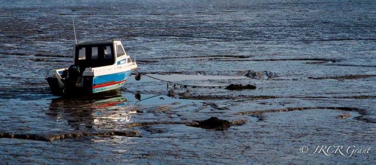 Boat and colours reflecting in the estuary mud at low tide
