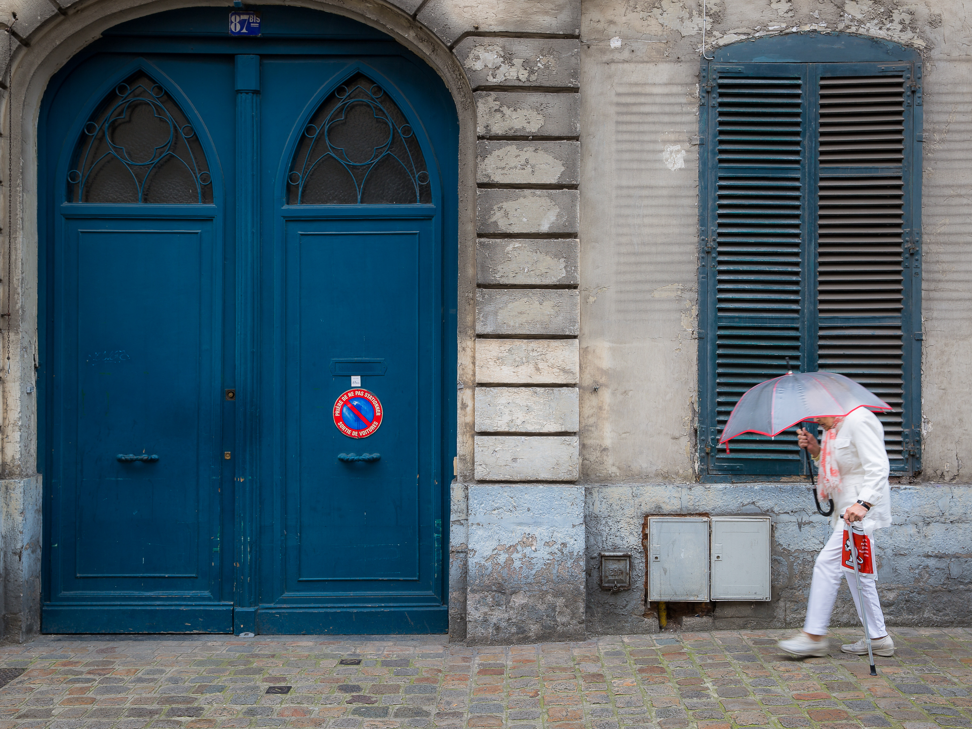 Lady walks across blue shutters and doors holding umbrella