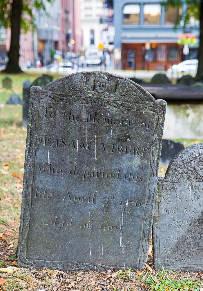 An old gravestone stands solid in the Granary burial ground as the City of Boston rushes by