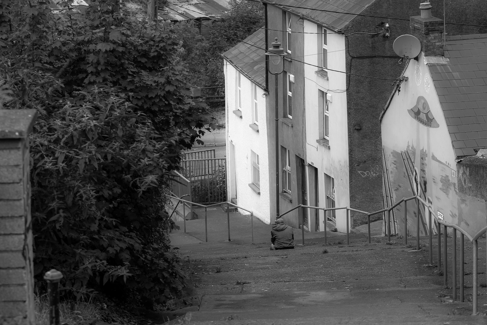 Man buries his head in hands while sitting on steps, smoking a cigarette
