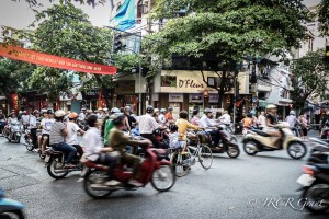 A cyclist walks her bicycle through a stream of mopeds in Hanoi, Vietnam