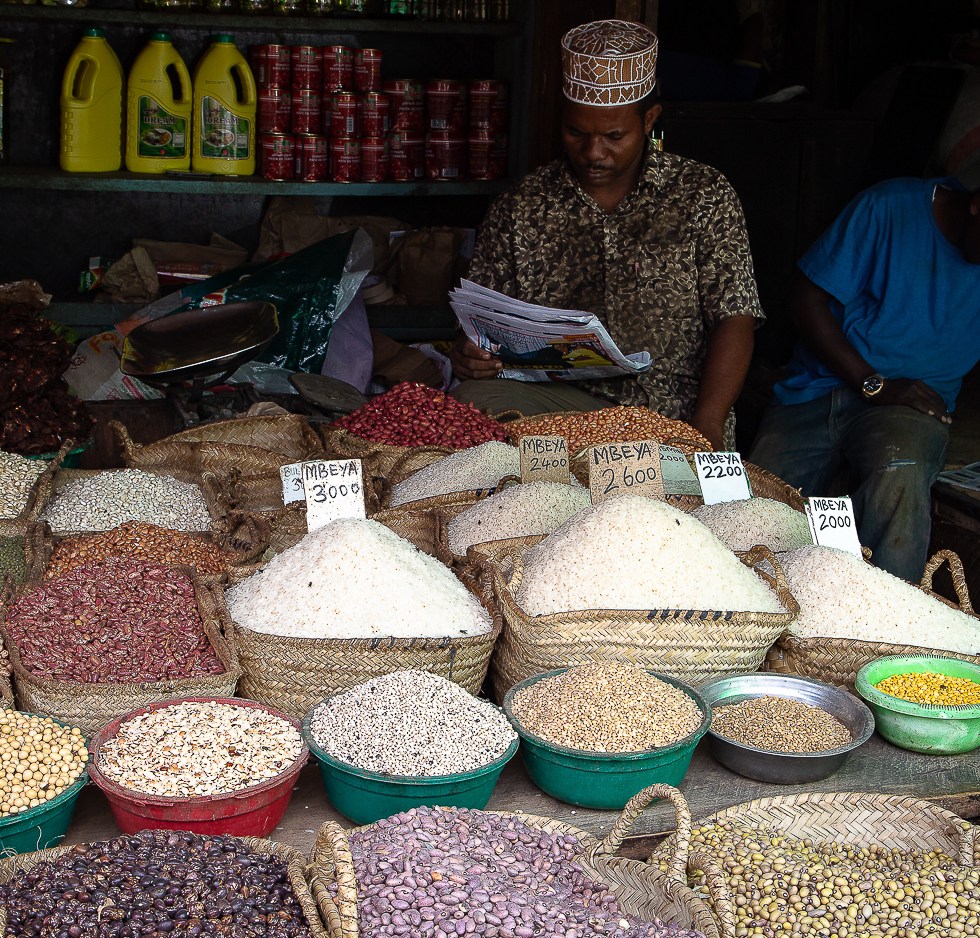 Two muslim stall holders read the daily paper in the dark shadows at the back of a pulse store, Stonetown, Zanzibar