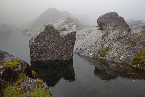 A boulder sits in the middle of a small lake, cast in mist