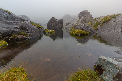 A large boulder sits in the middle of a mist shrouded corrie lough