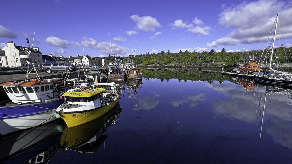 The harbour at Stornoway with moored colourful fishing boats resting on the flat calm waters, clouds being reflected perfectly on the waters surface.